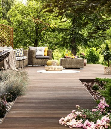 Beautiful wooden terrace with garden furniture surrounded by greenery on a warm, summer day